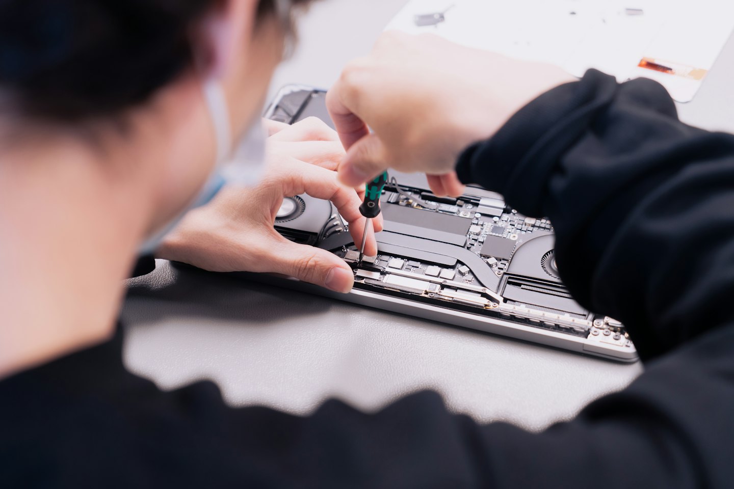 Technician repairing laptop components on a workbench.