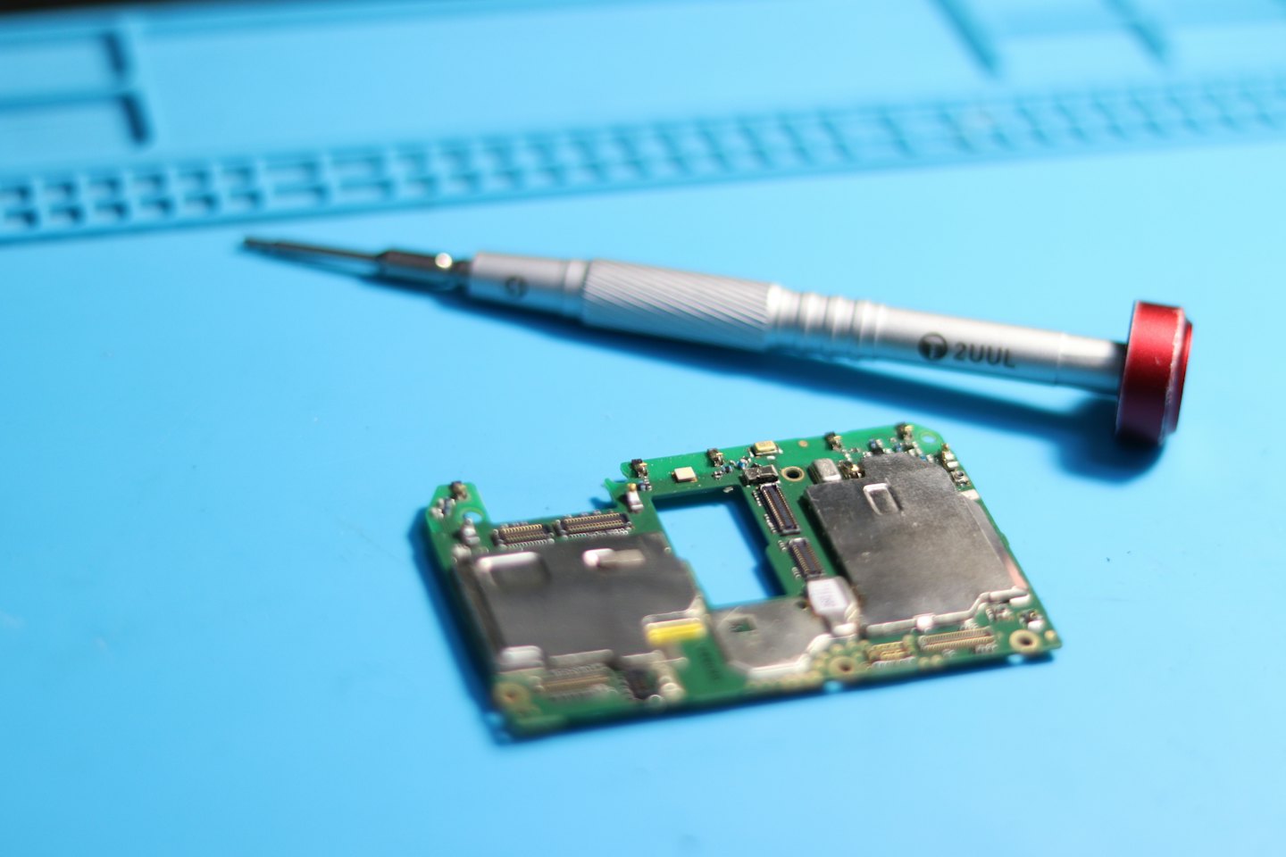 A precision screwdriver rests on a circuit board repair mat.